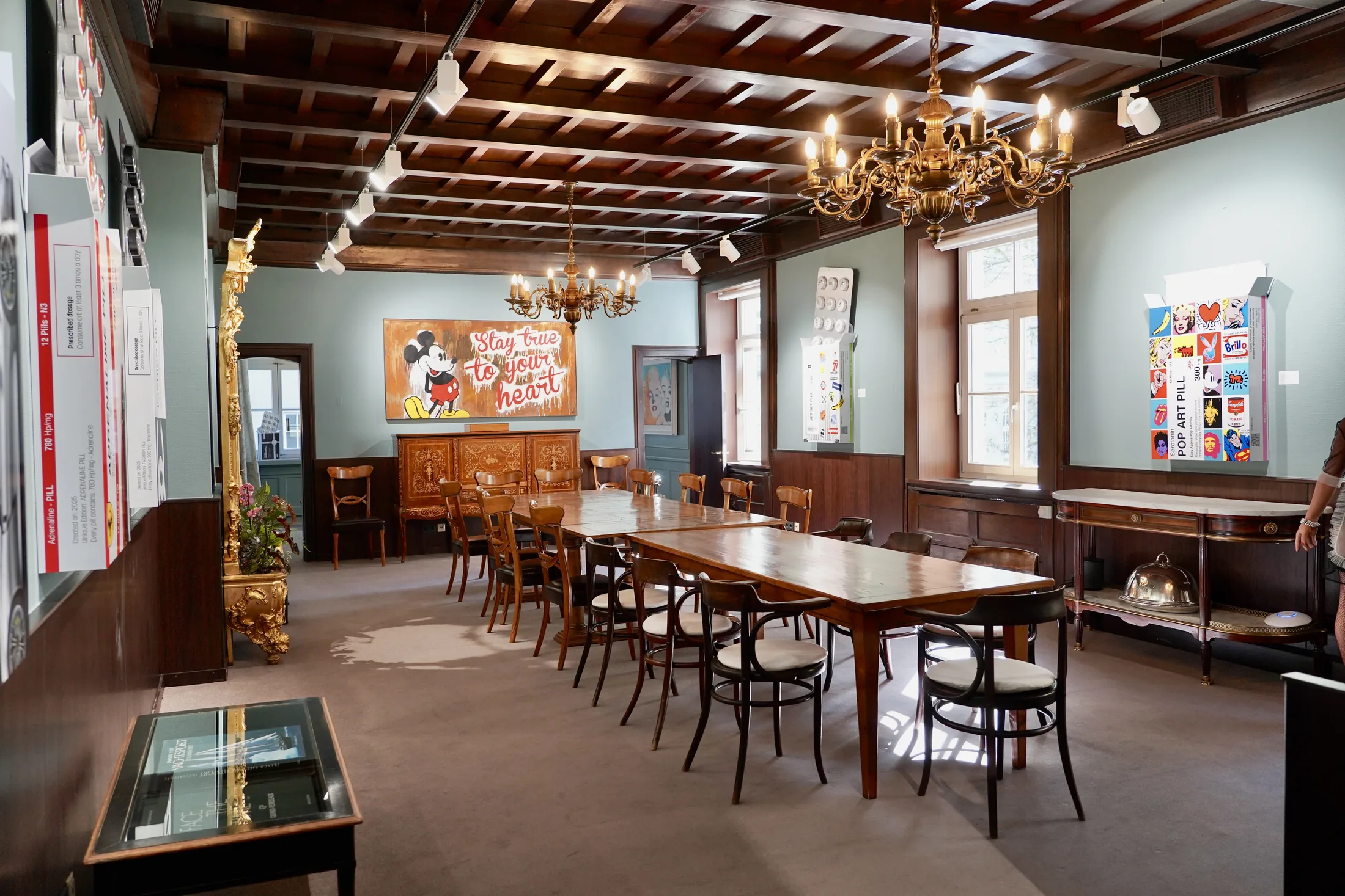 Historischer Galerieraum mit langem Holztisch, Kunstwerken und Kronleuchtern